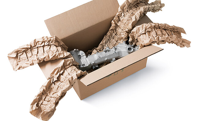 A cardboard box containing an engine component and brown paper cushioning